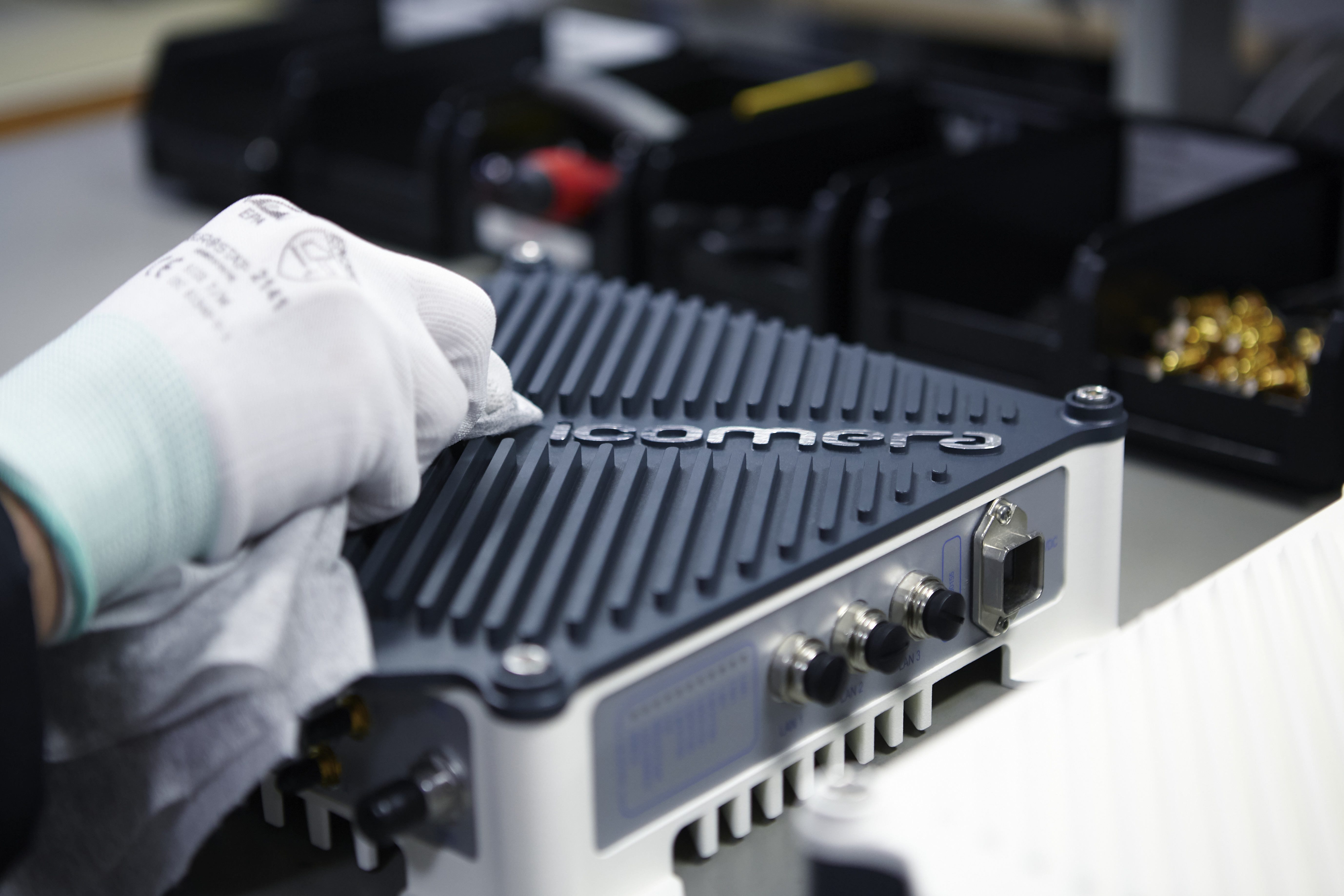 Photo of a gloved hand wiping an Icomera mobile connectivity and application router in a factory.
