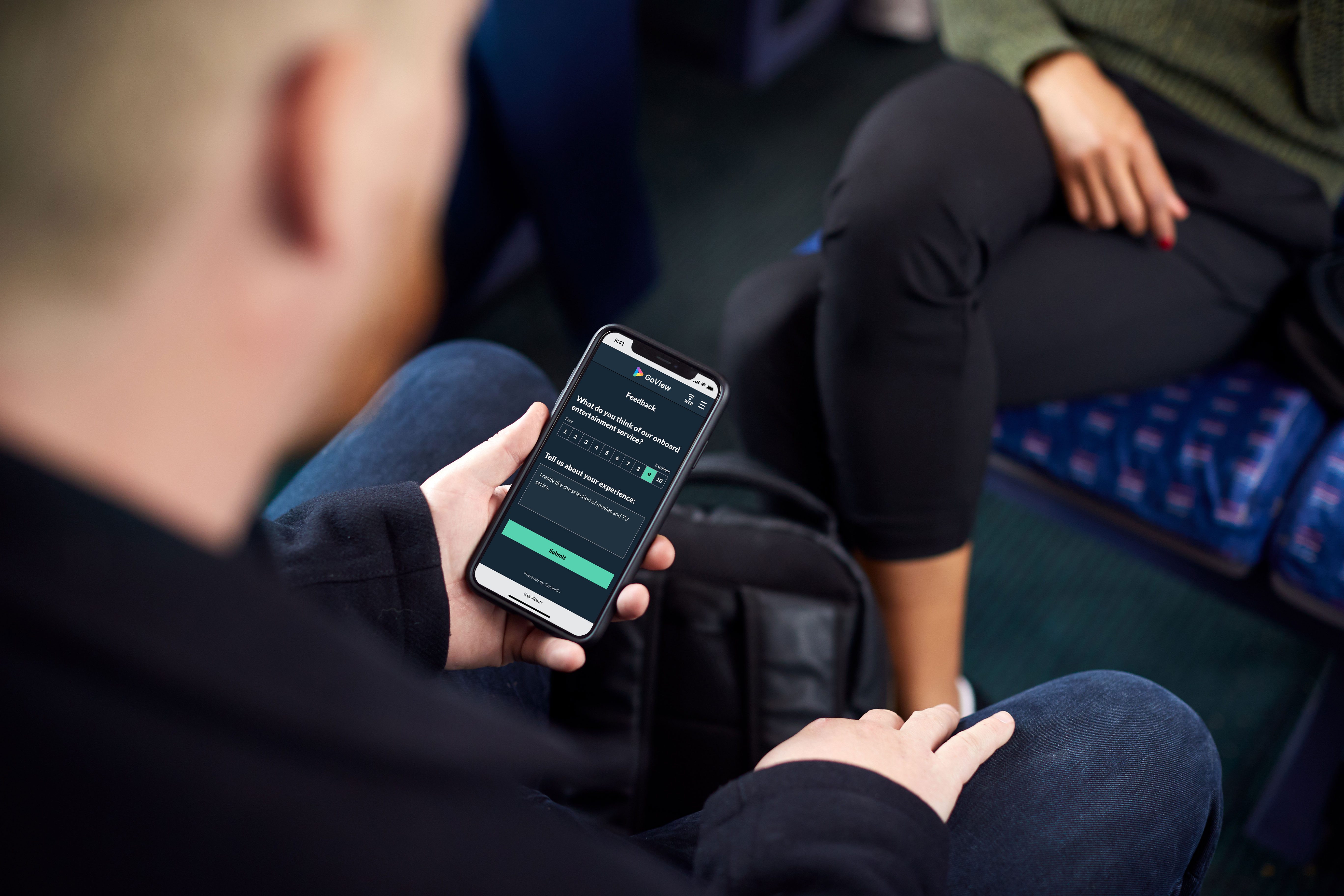 A male passenger provides feedback on a mobile phone, selecting 9 out of 10 for his satisfaction with the onboard entertainment service