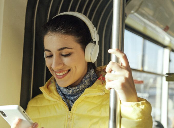 A female passenger wearing headphones and a yellow jacket receives real-time information to her smartphone