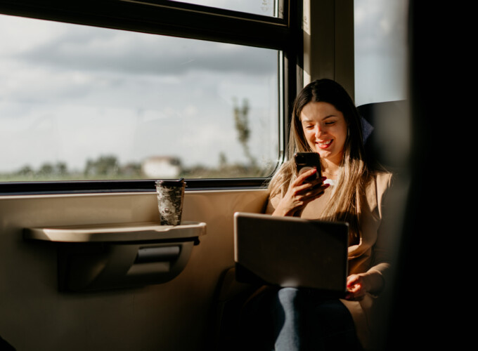 young woman travels by train, using lap top and mobile phone